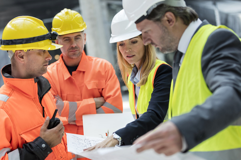 Ingenieure und Bauarbeiter bei der Überprüfung von Bauplänen auf der Baustelle, lizenzfreies Stockfoto