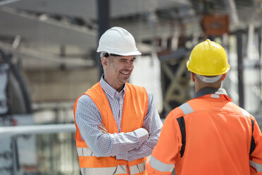 Smiling foreman talking to construction worker at construction site - CAIF10478