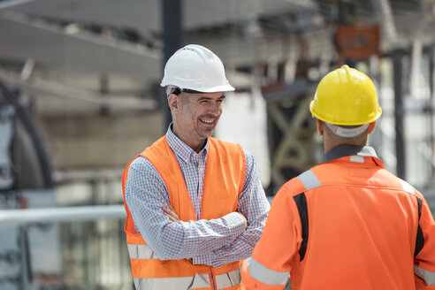 Lächelnder Polier im Gespräch mit einem Bauarbeiter auf der Baustelle - CAIF10478