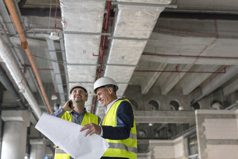 Männliche Ingenieure mit Taschenlampe und Bauplänen auf einer Baustelle - CAIF10479