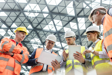 Foreman and construction workers using digital tablets in meeting at construction site - CAIF10483