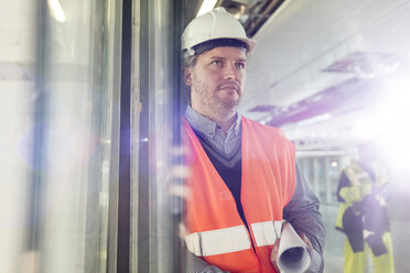 Seriöser männlicher Ingenieur mit Bauplänen auf einer Baustelle - CAIF10490