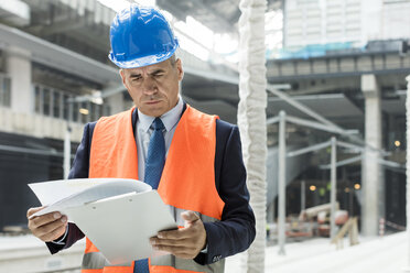 Businessman reviewing paperwork on clipboard at construction site - CAIF10493