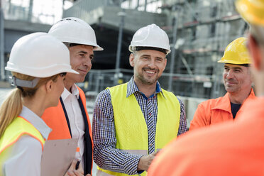 Smiling engineers and construction workers meeting at construction site - CAIF10495