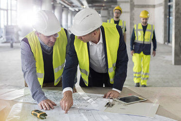 Male engineers discussing blueprints at construction site - CAIF10497