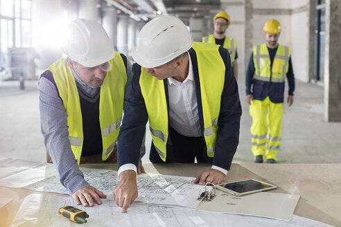 Männliche Ingenieure diskutieren auf einer Baustelle über Baupläne - CAIF10497