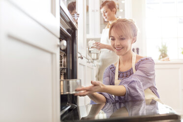 Lächelnde Frau beim Backen, die einen Kuchen in den Ofen schiebt - CAIF10507