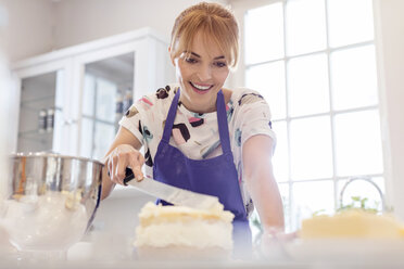 Lächelnde Frau, die in der Küche einen Schichtkuchen backt und glasiert - CAIF10513