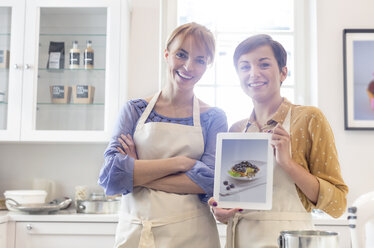 Porträt selbstbewusster weiblicher Gastronomen, die ein Foto von Lebensmitteln auf einem digitalen Tablet in der Küche zeigen - CAIF10518