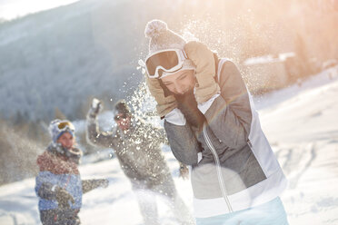 Verspielte Skifahrerfreunde bei einer Schneeballschlacht auf einem verschneiten Feld - CAIF10541