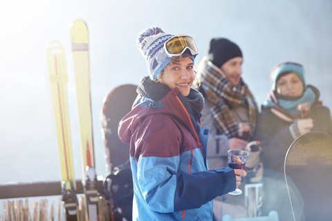 Porträt einer lächelnden Skifahrerin, die mit Freunden beim Apres-Ski einen Cocktail auf dem Balkon trinkt, lizenzfreies Stockfoto