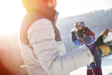 Freunde machen eine Schneeballschlacht auf einem sonnigen, verschneiten Feld - CAIF10550