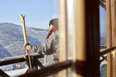 Männlicher Skifahrer mit Skiern auf dem sonnigen Kabinenbalkon - CAIF10559