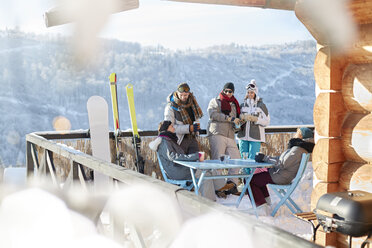 Skifahrer- und Snowboarder-Pärchen auf dem sonnigen Hüttenbalkon beim Après-Ski - CAIF10561