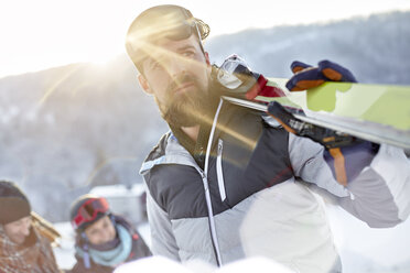 Männlicher Skifahrer mit Skiern in einem sonnigen Feld - CAIF10573