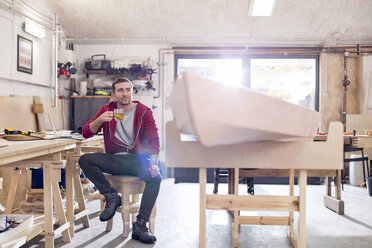 Männlicher Tischler trinkt Tee neben einem Holzboot in der Werkstatt - CAIF10574