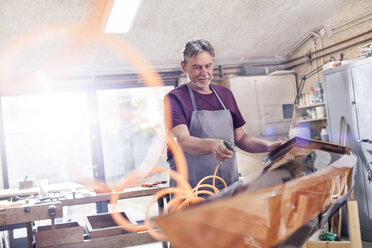 Männlicher Tischler mit Luftkompressor, der ein Holzkajak in der Werkstatt fertigstellt - CAIF10576