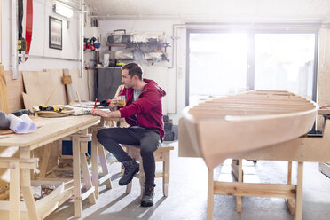 Männlicher Tischler trinkt Tee und arbeitet an einem Laptop auf einer Werkbank in einer Werkstatt - CAIF10577