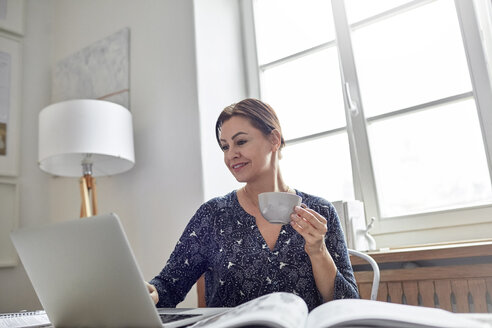 Lächelnde Geschäftsfrau trinkt Kaffee und arbeitet am Laptop - CAIF10582