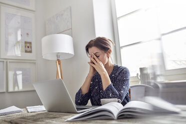 Tired, stressed businesswoman at laptop with head in hands - CAIF10588