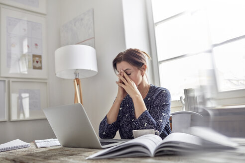 Müde, gestresste Geschäftsfrau am Laptop mit dem Kopf in den Händen - CAIF10588
