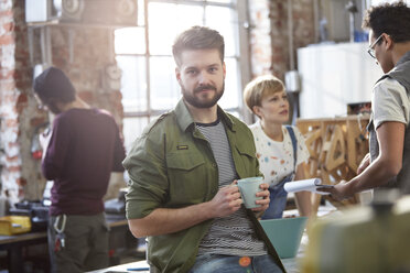 Porträt selbstbewusster junger männlicher Designer beim Kaffeetrinken in einer Werkstatt - CAIF10593