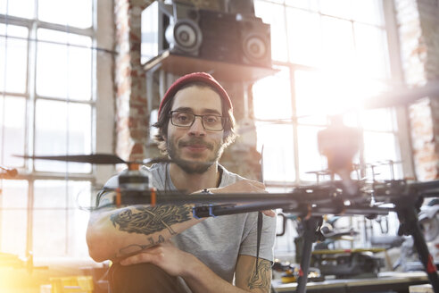 Porträt selbstbewusster männlicher Designer mit Tätowierungen bei der Arbeit an einer Drohne in einer Werkstatt - CAIF10614