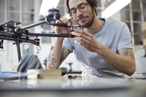 Männlicher Designer mit Tätowierungen beim Zusammenbau einer Drohne in einer Werkstatt - CAIF10623