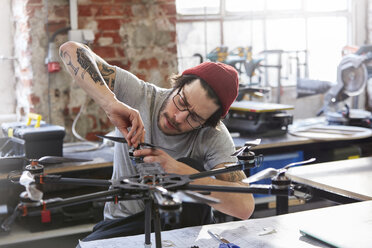 Männlicher Designer mit Tätowierungen beim Zusammenbau einer Drohne in einer Werkstatt - CAIF10631