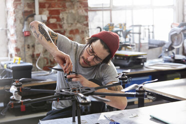 Male designer with tattoos assembling drone in workshop - CAIF10631