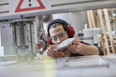 Male designer wearing ear protectors, examining prototype in workshop - CAIF10640