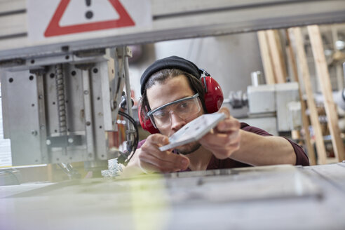Männlicher Designer mit Gehörschutz, der in der Werkstatt einen Prototyp untersucht - CAIF10640