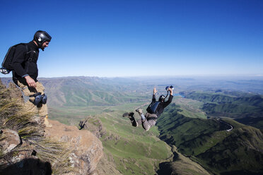 Mann schaut auf einen Freund, der seinen Fallschirm öffnet, während er auf einem Berg steht - CAVF05201