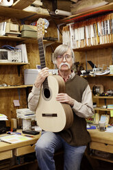 Porträt eines Mannes mit Gitarre in einer Werkstatt - CAVF05300