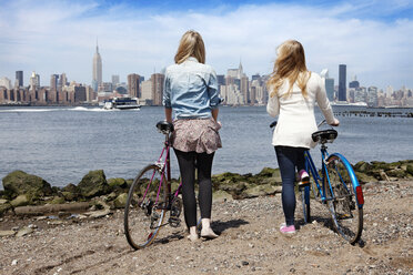 Rear view of friends with bicycle at riverbank - CAVF05362