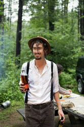 Mann hält Bärenflaschen und schaut weg, während er im Wald steht - CAVF05401
