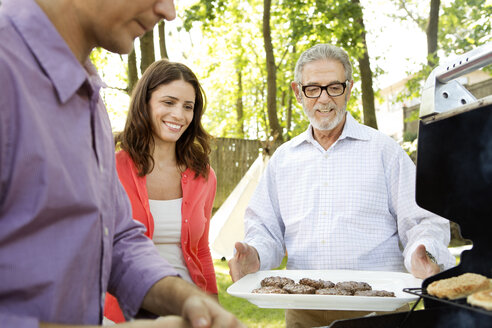 Glückliche Familie beim Grillen auf dem Rasen - CAVF05434