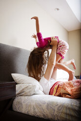 Father lifting girl while lying on bed at home - CAVF05440