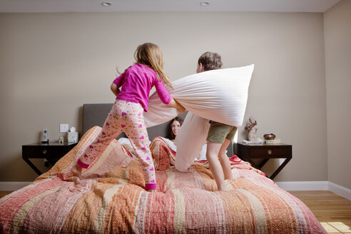 Kinder spielen Kissenschlacht mit Eltern auf dem Bett zu Hause - CAVF05443