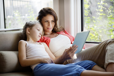 Frau unterrichtet Tochter, während sie sich zu Hause auf dem Sofa entspannt - CAVF05447