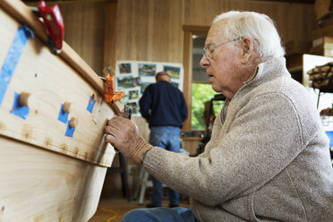 Seitenansicht eines Senioren bei der Arbeit an einem Kanu in der Werkstatt - CAVF05454