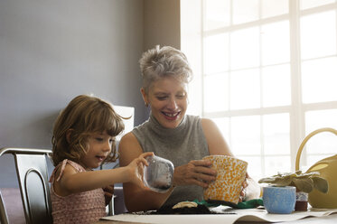 Glückliche Frau mit Enkelin pflanzt Bäumchen in Topf zu Hause - CAVF05469