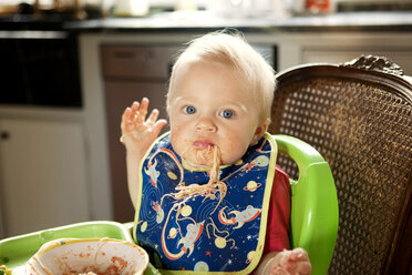Portrait of baby boy eating noodles while sitting on high chair at home - CAVF05524