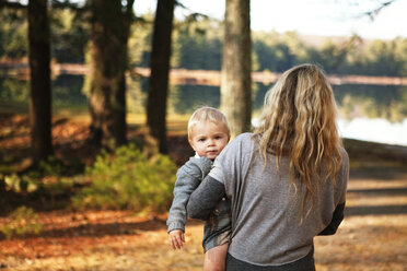 Rear view of woman carrying baby while walking on field - CAVF05533