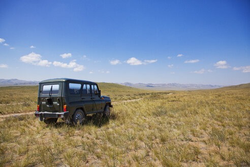 Auto auf grasbewachsenem Feld gegen blauen Himmel - CAVF05544