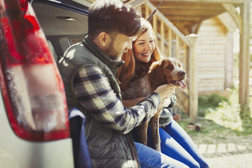 Couple petting pet dog at back of car - CAIF10695