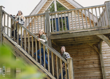 Friends climbing staircase outside wooden cabin - CAIF10697