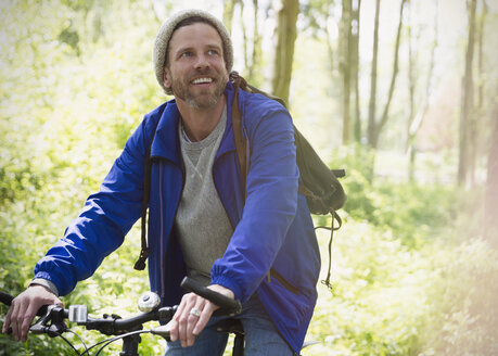 Smiling man mountain biking in woods - CAIF10700