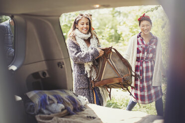 Smiling woman loading backpack into back of car - CAIF10701