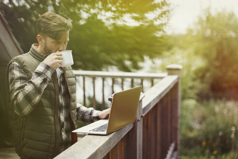 Mann trinkt Kaffee und benutzt Laptop auf dem Kabinendeck - CAIF10702